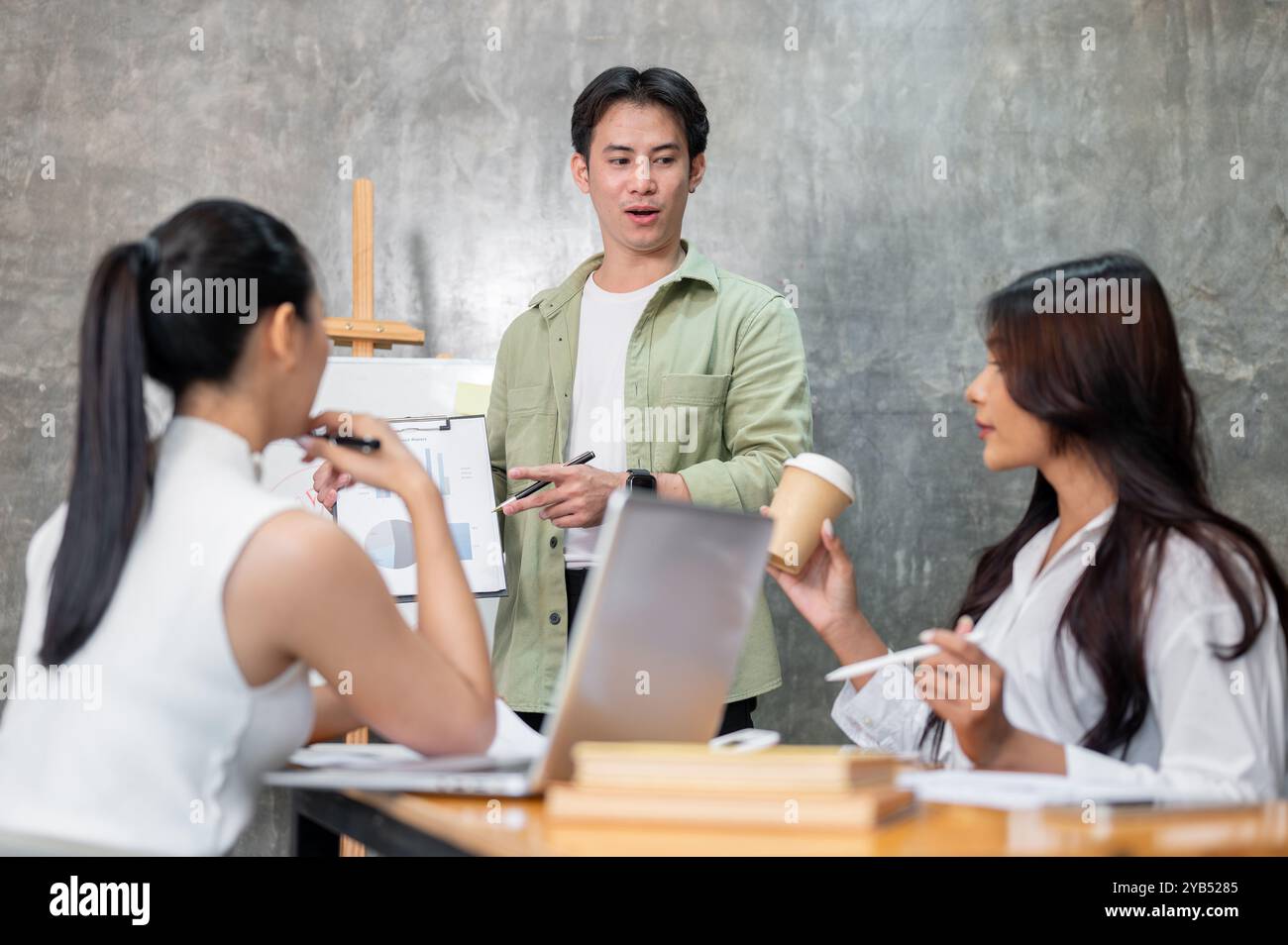 Un bel homme d'affaires asiatique intelligent dans une tenue décontractée dirige la réunion, parle à son équipe et partage ses idées sur un projet à venir. Banque D'Images