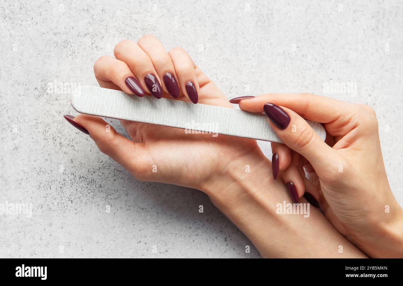 Une personne remplit soigneusement ses ongles à la maison, en utilisant une lime à ongles pour façonner et lisser les bords, créant un look élégant pour une manucure. Banque D'Images