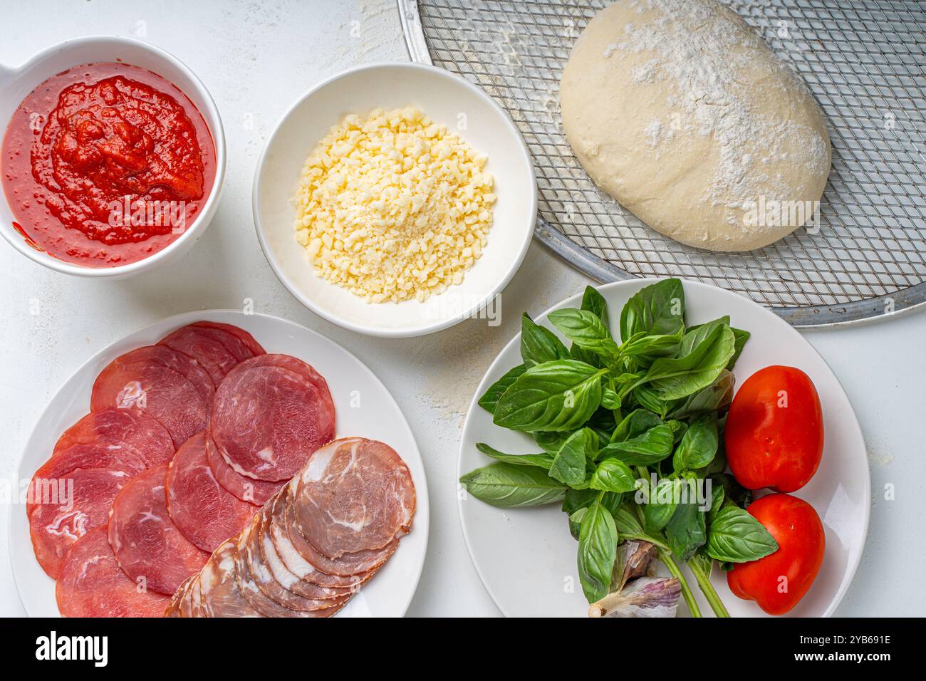 Ingrédients pour la fabrication de pizza italienne : pâte, sauce tomate, parmesan, tomates, basilic, ail, saucisse sur une table blanche. Vraie recette de pizza. Haute qualité Banque D'Images