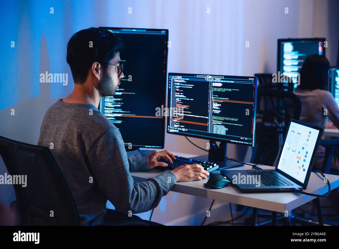 Développeurs de logiciels asiatiques travaillant sur plusieurs écrans affichant le code et les diagrammes d'application la nuit dans le bureau moderne Banque D'Images