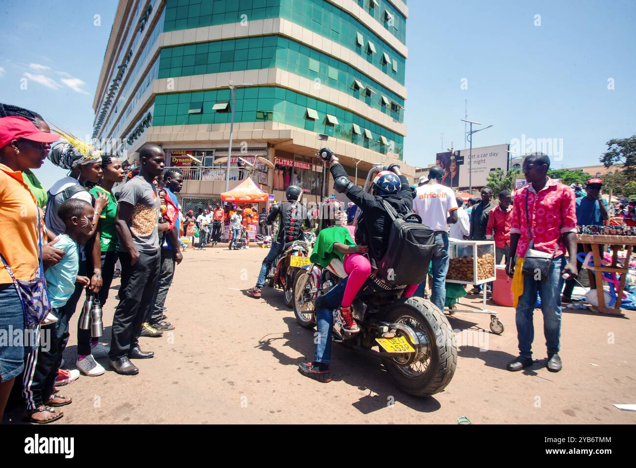 Un jeune homme porte une femme sur une moto dans la rue pendant le carnaval de Kampala Banque D'Images