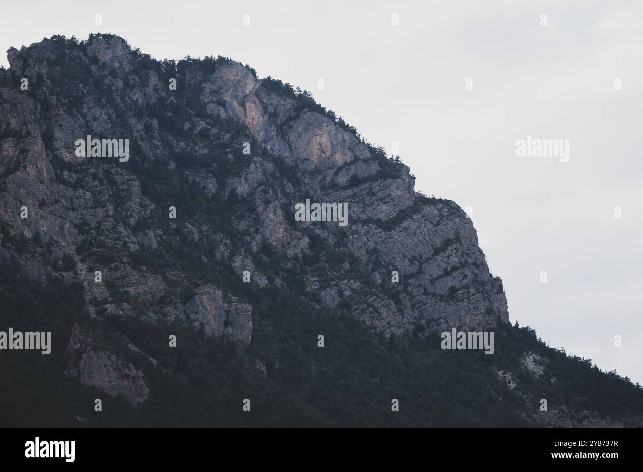 Vue sur une montagne escarpée avec des falaises rocheuses et une forêt dense, offrant un contraste entre le rocher nu et la verdure de la végétation. Banque D'Images