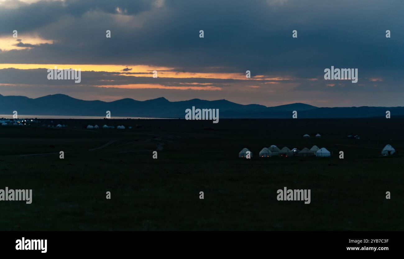 Les rayons du soleil traversent les nuages et les colorent. Au premier plan se trouvent des yourtes blanches. Des lumières de nuit étaient allumées dans certaines yourtes. Banque D'Images