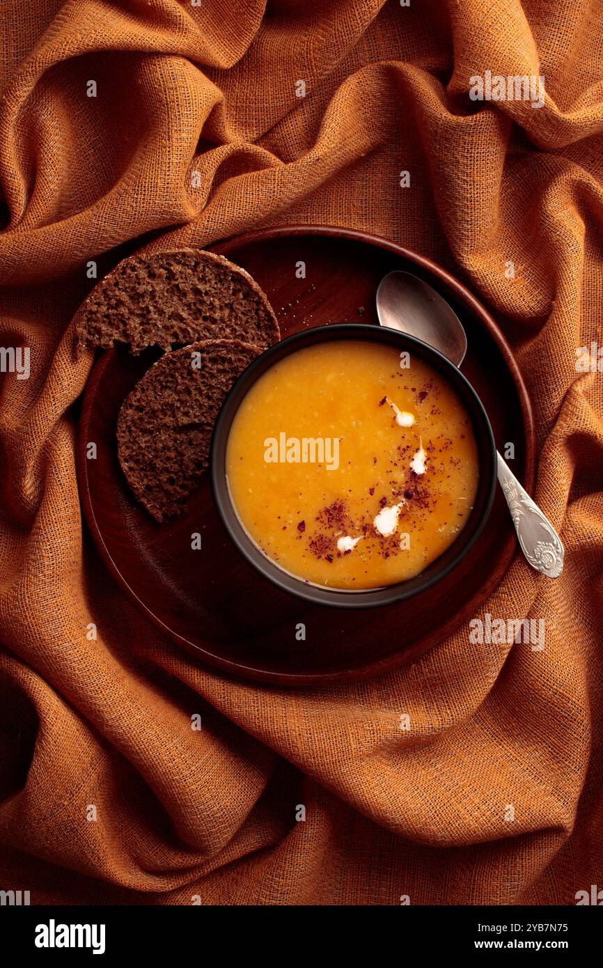 Soupe de citrouille à la crème dans un bol noir et assiette en bois sur fond textile brun. Gros plan. Vue de dessus avec espace de copie. Récolte d'automne Banque D'Images