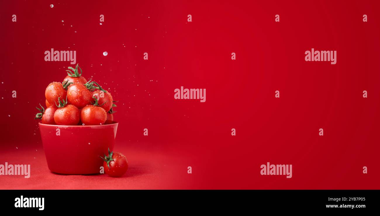 Concept alimentaire créatif. Motif tomates. Tomates cerises juteuses rouges mûres dans un bol rouge avec des gouttes d'eau sur fond rouge. Végétalien frais sains bio fo Banque D'Images