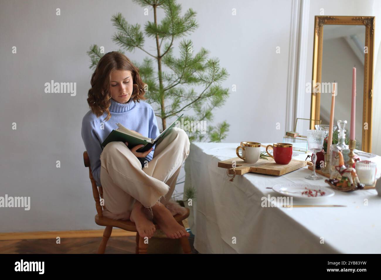 Une fille assise tranquillement avec un livre dans les mains, feuilletant un vieil album photo alors qu'elle se prépare à accueillir le nouvel an et Noël Banque D'Images