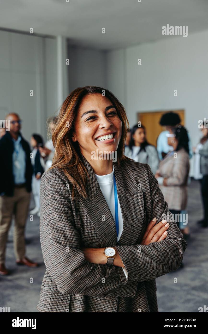 Leader féminin confiant souriant dans un environnement d'affaires diversifié. Les bras croisés, elle met en valeur l'autonomisation, le travail d'équipe et le succès de l'entreprise. Banque D'Images