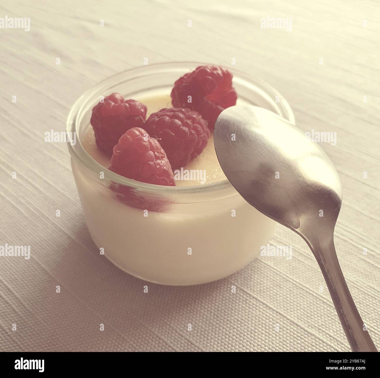 La crème aux oeufs est un dessert traditionnel français composé d’œufs, de lait et de vanille. C'est dans un ramequin avec quatre framboises et une cuillère sur le dessus Banque D'Images