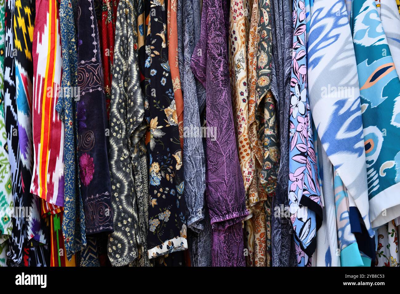 Robes multicolores ouzbèkes traditionnelles et gilets avec des motifs nationaux sur des cintres dans une rangée à vendre. Khiva. Ouzbékistan. Banque D'Images