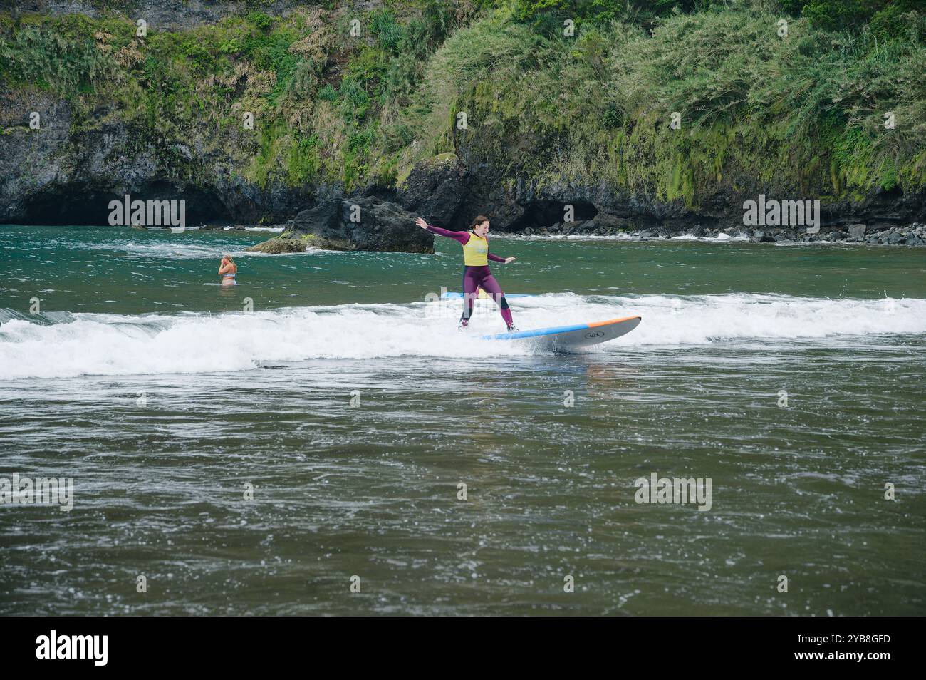Une jeune surfeuse se balance sur sa planche tout en chevauchant une petite vague pendant une leçon de surf à la plage de Seixal Banque D'Images