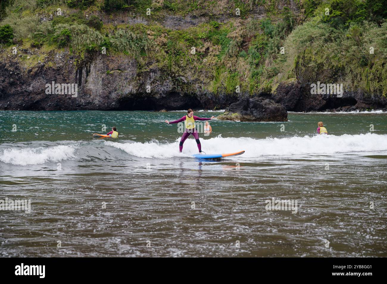Une jeune surfeuse se balance sur sa planche tout en chevauchant une petite vague lors d’une session d’école de surf à la plage de Seixal Banque D'Images