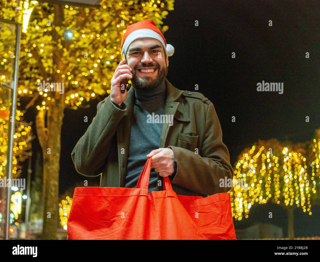 Homme barbu utilisant son téléphone tout en regardant son sac à provisions pendant la période de Noël Banque D'Images