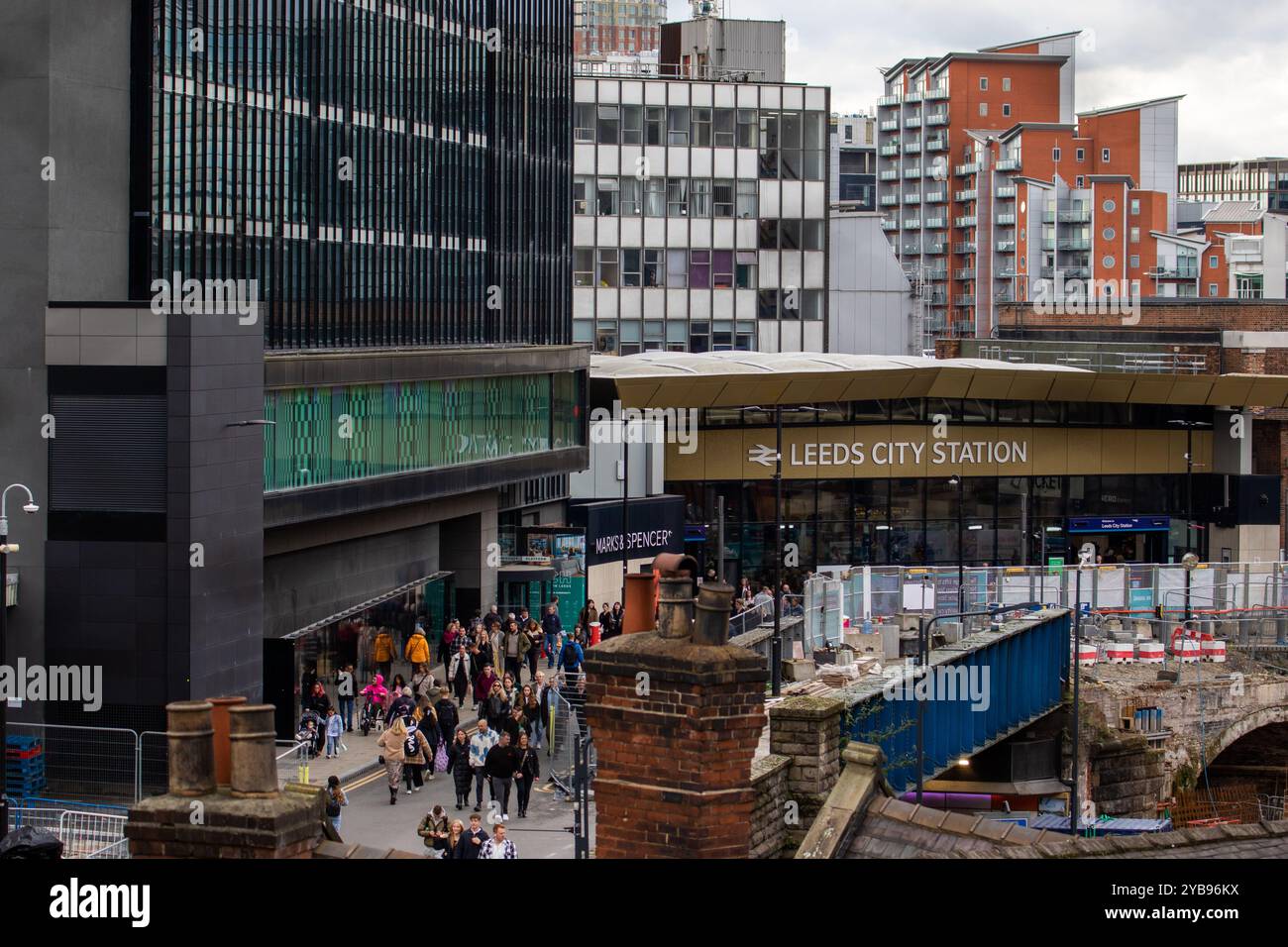 Une scène de rue animée en face de Leeds City Station avec une foule de gens qui passent devant l'entrée. La façade de la gare dispose d'un grand panneau avec Banque D'Images