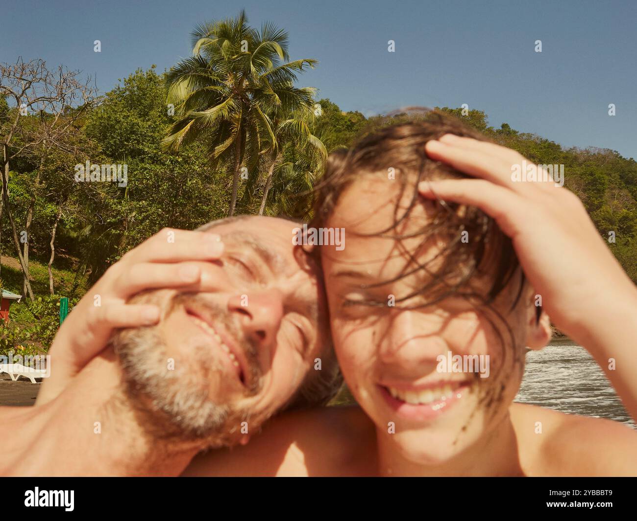 Portrait heureux père et fils riant et serrant sur la plage ensoleillée, Saint Vincent et les Grenadines Banque D'Images