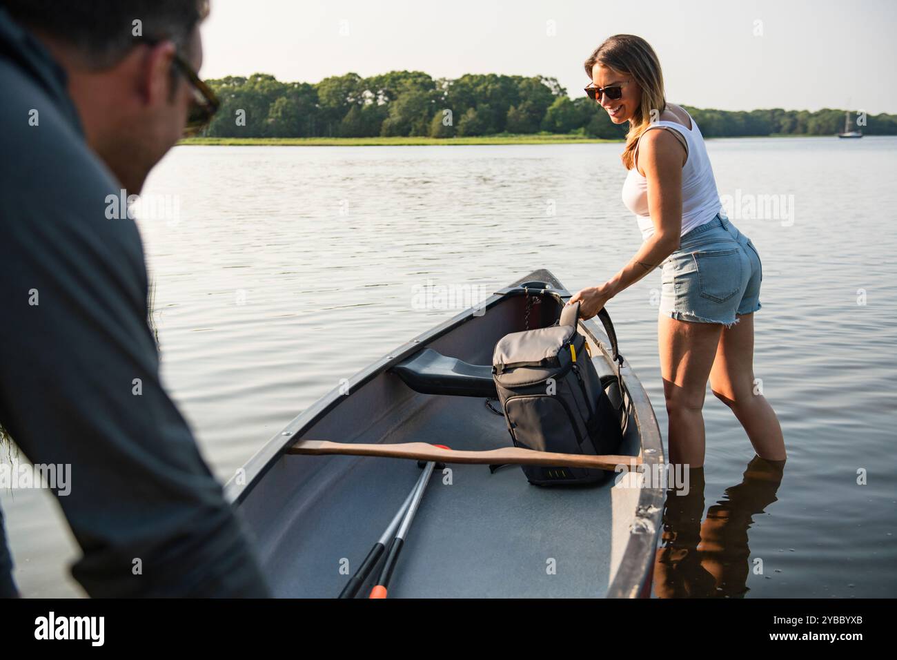 Femme souriante chargeant le sac à dos dans le canoë le jour d'été Banque D'Images