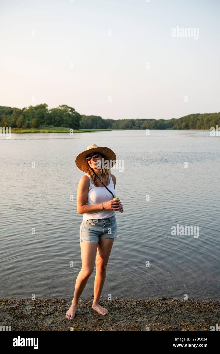 Femme pataugant dans l'eau peu profonde avec boisson le jour d'été Banque D'Images