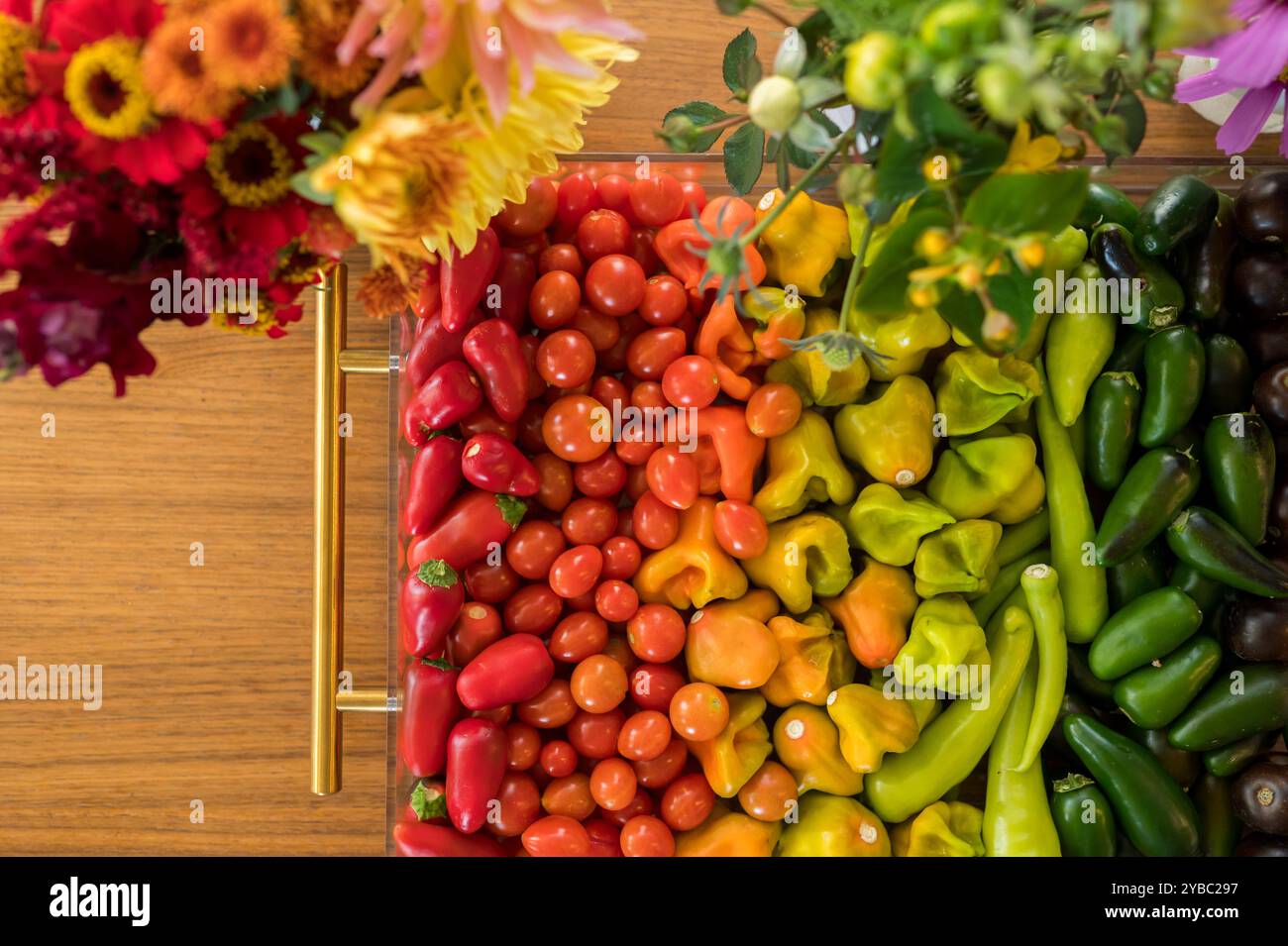 Légumes et fleurs colorés disposés dans des tons arc-en-ciel sur une table en bois Banque D'Images