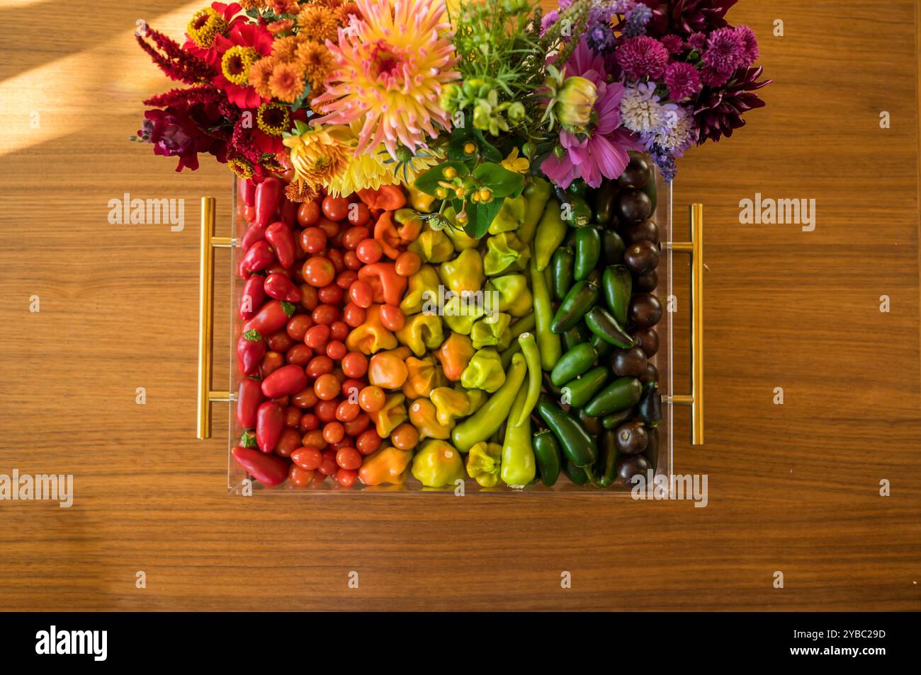 Légumes et fleurs colorés disposés dans des tons arc-en-ciel sur une table en bois Banque D'Images