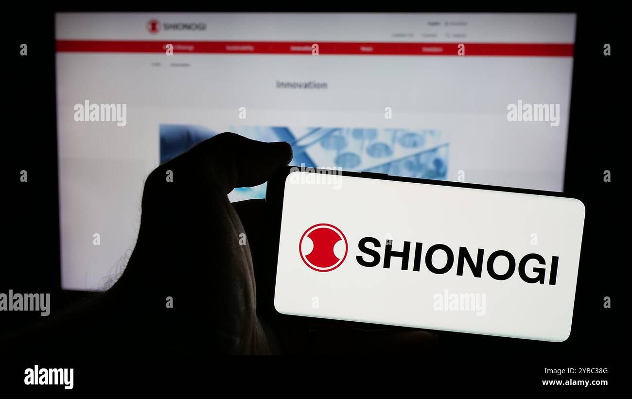 Personne tenant le téléphone portable avec le logo de la société pharmaceutique japonaise Shionogi Co. Ltd sur l'écran en face de la page Web. Concentrez-vous sur l'affichage du téléphone. Banque D'Images