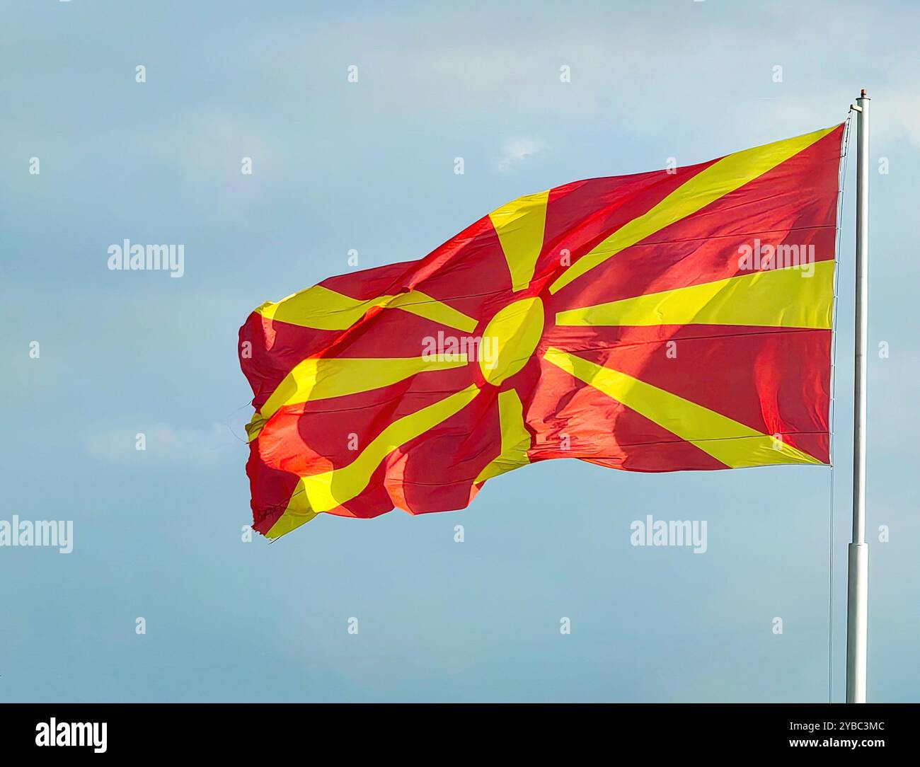 Drapeau macédonien agitant dans le vent : couleurs nationales rouge et jaune contre un ciel bleu clair Banque D'Images