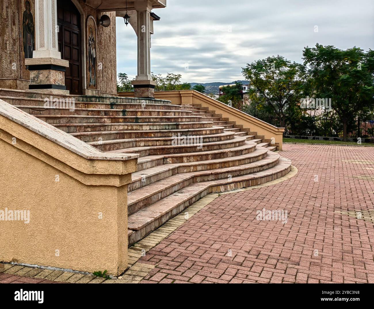 Escalier courbé en béton menant à la porte brune en bois : partie de l'architecture de l'église orthodoxe macédonienne avec des piliers, ciel nuageux, jour couvert Banque D'Images