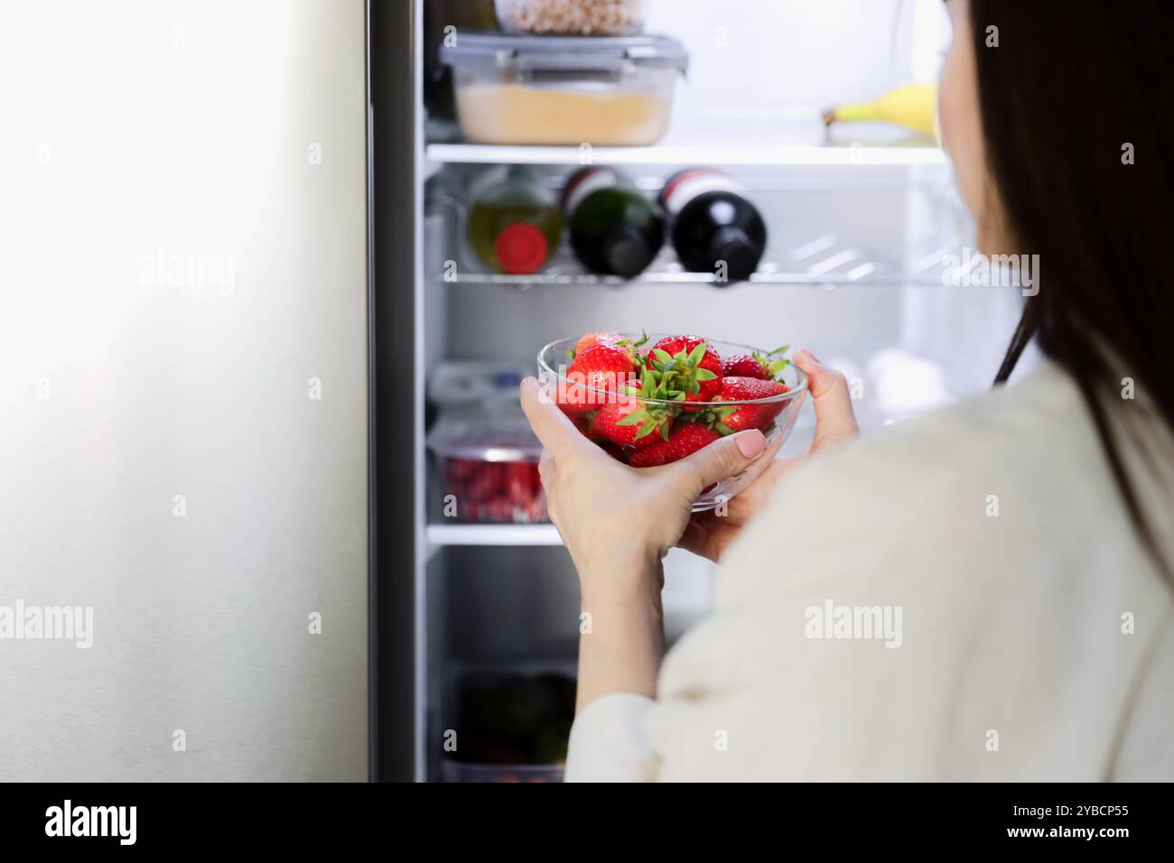 Jeune femme enceinte affamée debout devant un réfrigérateur ouvert, prend la fraise du réfrigérateur, gros plan. Grossesse saine manger. Je cherche de la nourriture Banque D'Images