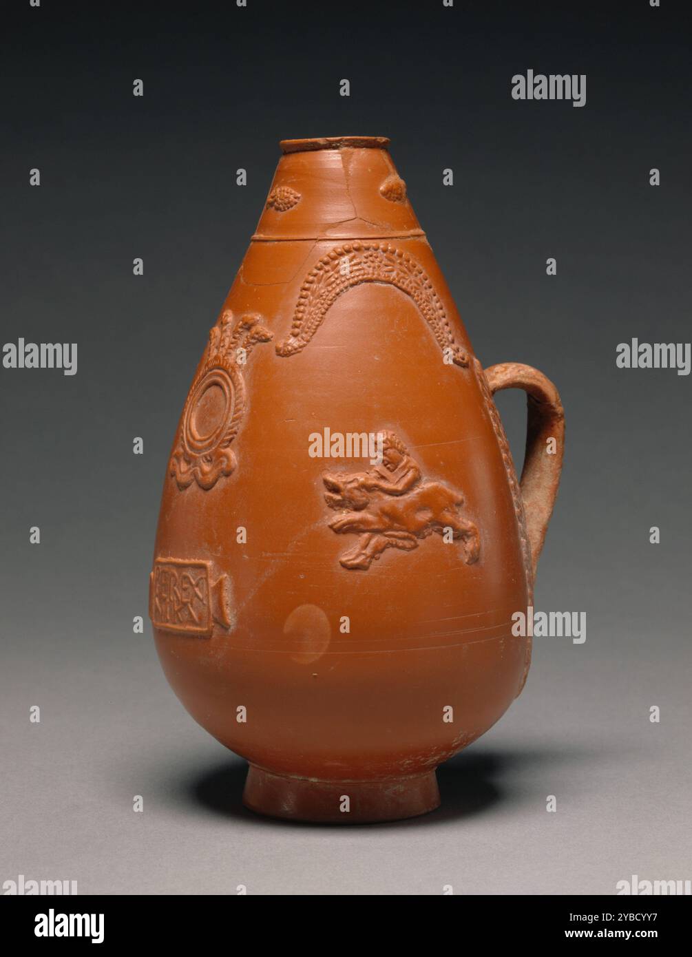 Carafe Pyriform Red-Slip, A.D. 200-275. Informations supplémentaires : pichet pyriforme rouge, avec pied circulaire, décoré tout autour par des scènes tirées des chasses aux bêtes sauvages (Venationes) mises en scène dans des amphithéâtres. Les principaux motifs décoratifs sont répartis sur deux zones verticales. Deux scènes de venatores (chasseurs professionnels) luttant avec des sangliers, enjambées par des éléments ornementaux arqués. En face de la poignée, et entre les deux scènes de Venatio, est une couronne avec cinq panaches verticaux, emblèmes de l'équipe acclamés dans une tabula ansata ci-dessous, où l'inscription "Perexi Nik Banque D'Images