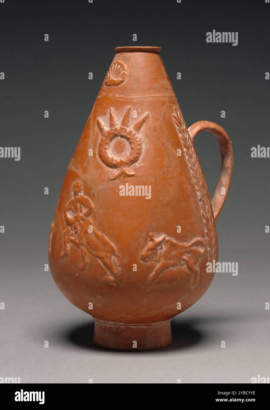 Carafe Pyriform Red-Slip, A.D. 200-275. Informations supplémentaires : pichet pyriforme rouge, avec pied circulaire, décoré tout autour de scènes tirées des chasses aux bêtes sauvages (venationes) mises en scène dans des amphitéateurs. Les motifs décoratifs sont répartis sur deux zones verticales, chacune présentant deux représentations, placées l'une au-dessus de l'autre. A droite de la poignée : un chasseur qui s'agresse avec un cheval, et un archer qui vise avec un arc. A gauche : un troisième chasseur combattant un sanglier, tandis que deux sangliers courent à proximité ; au-dessus, une couronne de victoire ornée de pointes renversées, emblèmes de l'équipe. La poignée elle-même est flanquée Banque D'Images