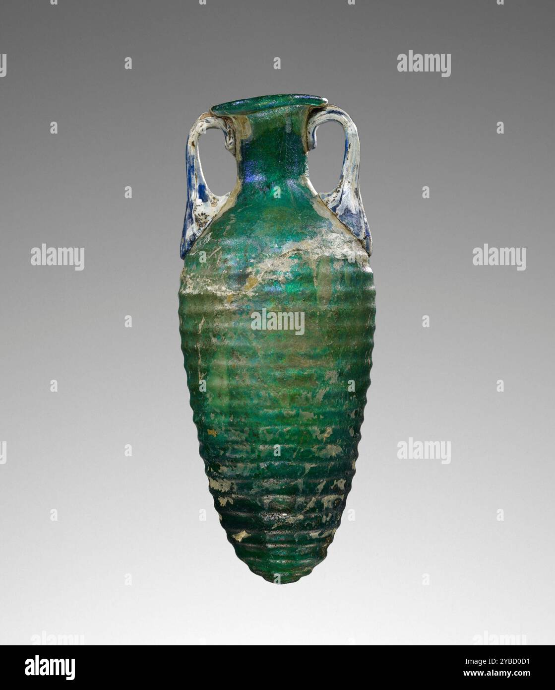 Amphoriskos, 1st Century A.D. informations supplémentaires : amphoriskos soufflé par moule de verre vert foncé soufflé dans un moule en deux parties. Le corps conique est décoré de vingt-trois arêtes horizontales. Le col cylindrique court se termine par une bouche évasée et une lèvre repliée vers l'intérieur. Deux petites poignées bleues ont été appliquées sur l'épaule et tirées jusqu'au bord. Cet amphoriskos est sévèrement altéré et a été remonté avec de gros remplissages sur le corps. Banque D'Images