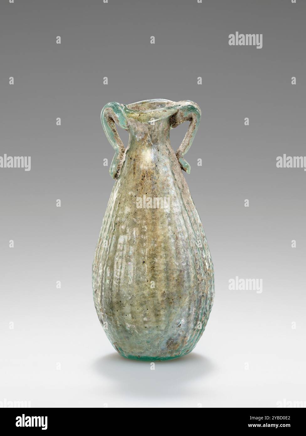 Panier Amphoriskos, 1st Century A.D. informations supplémentaires : ce panier amphoriskos soufflé par moule est fait de verre bleu pâle (apparaît vert dans un peu de lumière). Son corps en forme de goutte d'eau avec une base aplatie est décoré d'un motif de panier. La marque de couture indique que cet amphoriskos a été soufflé dans un moule en deux parties. Le col cylindrique court se termine par une bouche évasée et une lèvre repliée vers l'intérieur. Deux petites poignées "flottantes" ont été appliquées sur la jante. La surface est irisée à l'intérieur et présente quelques accrétions brunâtres autour des poignées. Banque D'Images