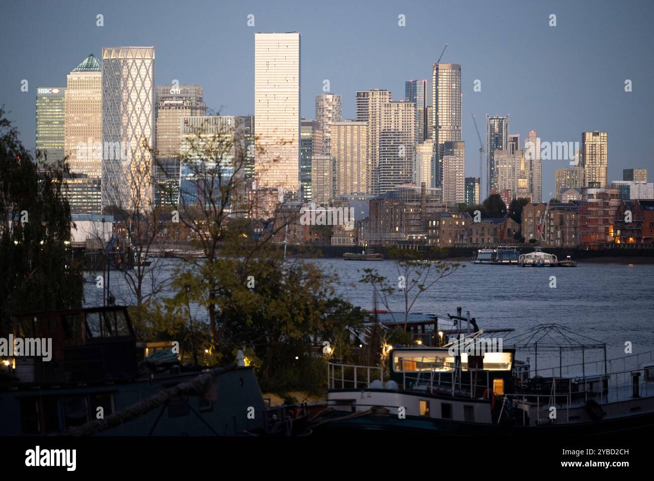 Les grands gratte-ciel d'entreprise de Canary Wharf dans les Docklands de Londres sont vus au-delà de la communauté des péniches de 'Tower Bridge Moorings' sur la Tamise, le 17 octobre 2024, à Londres, en Angleterre. Tower Bridge Moorings est le seul jardin flottant de la capitale - un mode de vie durable pour une communauté de plus de cent adultes et enfants, et un abri pour la faune sur la rivière. Tower Bridge Moorings est le seul jardin flottant de la capitale - un mode de vie durable pour une communauté de plus de cent adultes et enfants, et un abri pour la faune sur la rivière. Banque D'Images