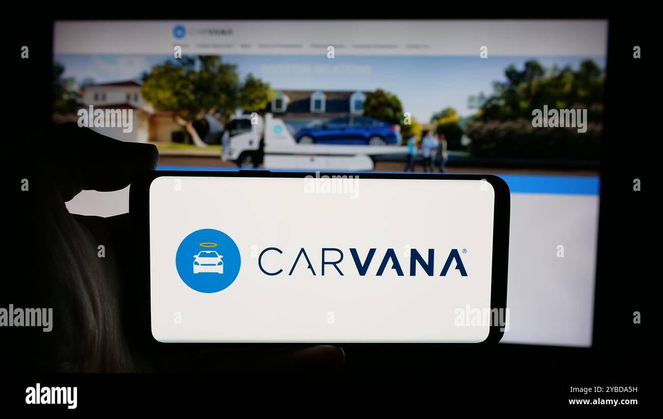 Personne tenant le téléphone portable avec le logo de la société de vente au détail de voiture usagée des États-Unis Carvana Co. sur l'écran en face de la page Web d'affaires. Concentrez-vous sur l'affichage du téléphone. Banque D'Images