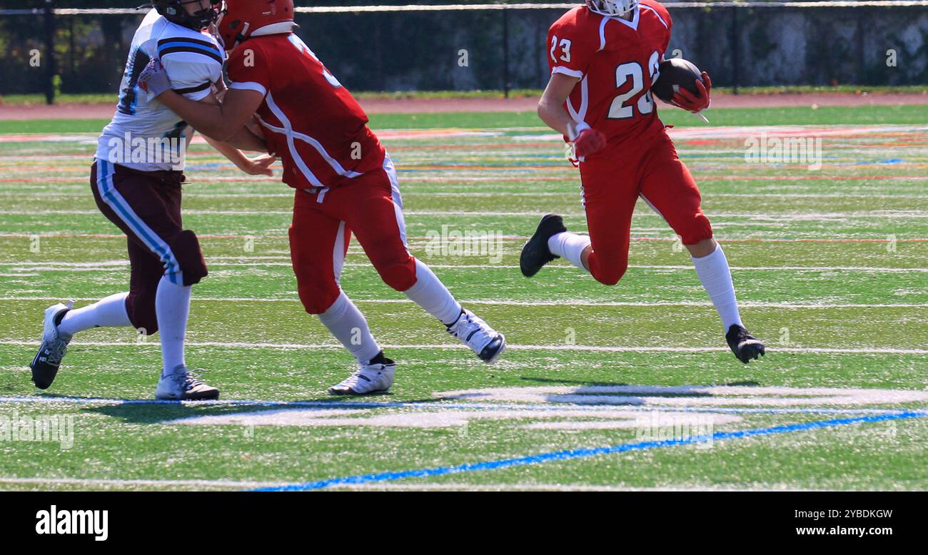 Vue de face d'un joueur de football qui court derrière son bloqueur sur le terrain pendant un match de football au lycée. Banque D'Images