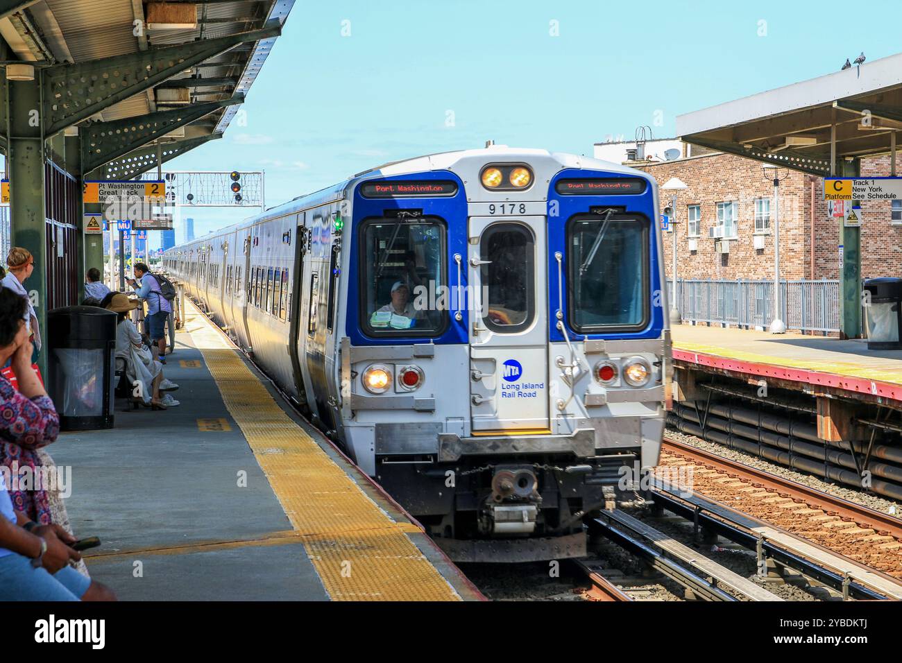 Queens, New Yok, États-Unis - 20 août 2024 : un train s'arrête dans une gare animée, avec des passagers qui attendent et profitent de la journée ensoleillée. Banque D'Images