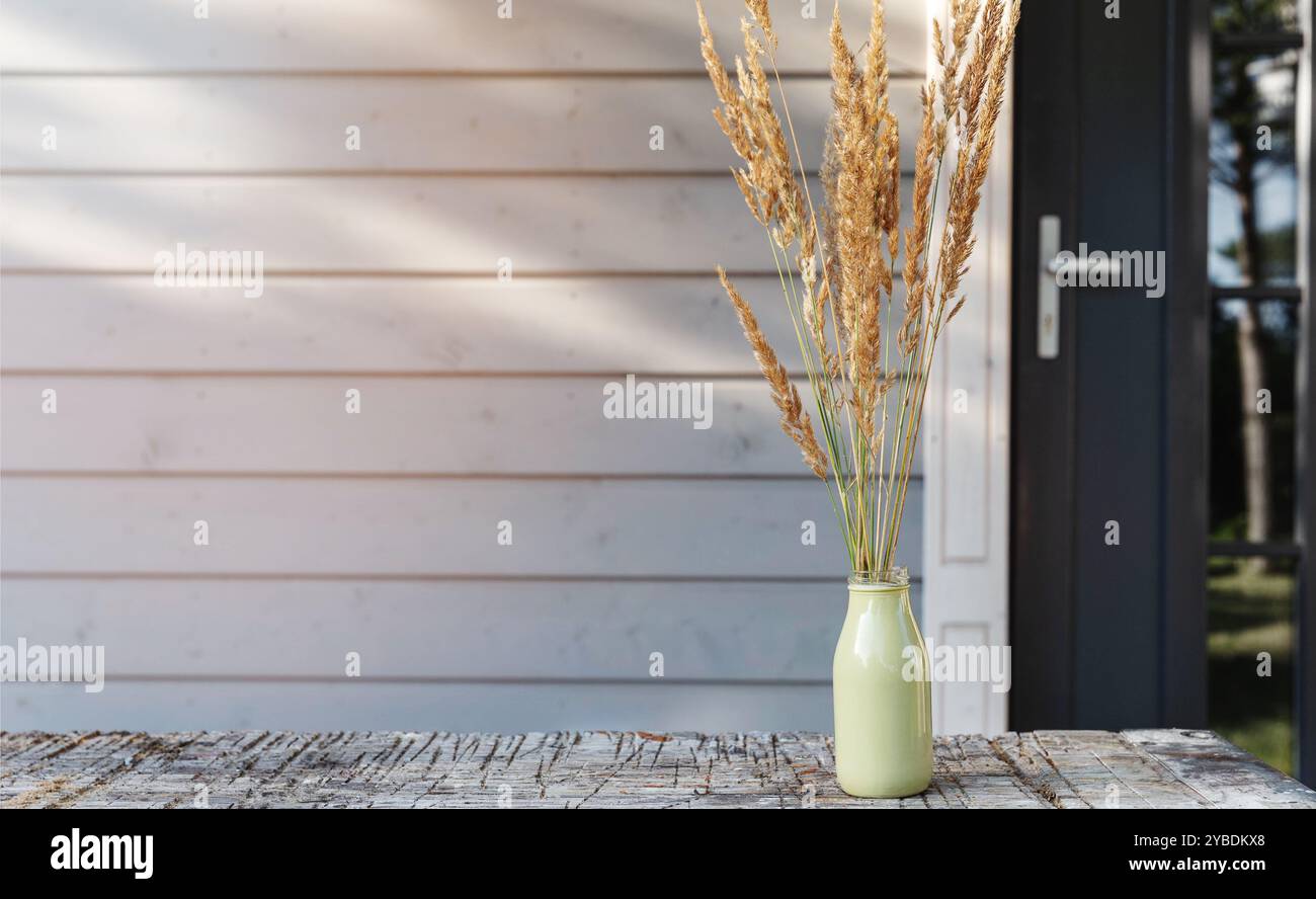 Carte d'affiche, herbes d'automne sur la table en bois contre la porte et le mur de la maison moderne en bois. Banque D'Images