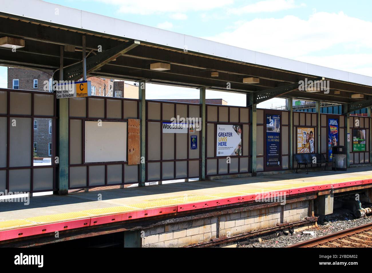 Queens, New York, États-Unis - 20 août 2024 : un après-midi tranquille à la gare de Woodside avec des bancs vides et des panneaux de la gare sous un ciel bleu. Banque D'Images