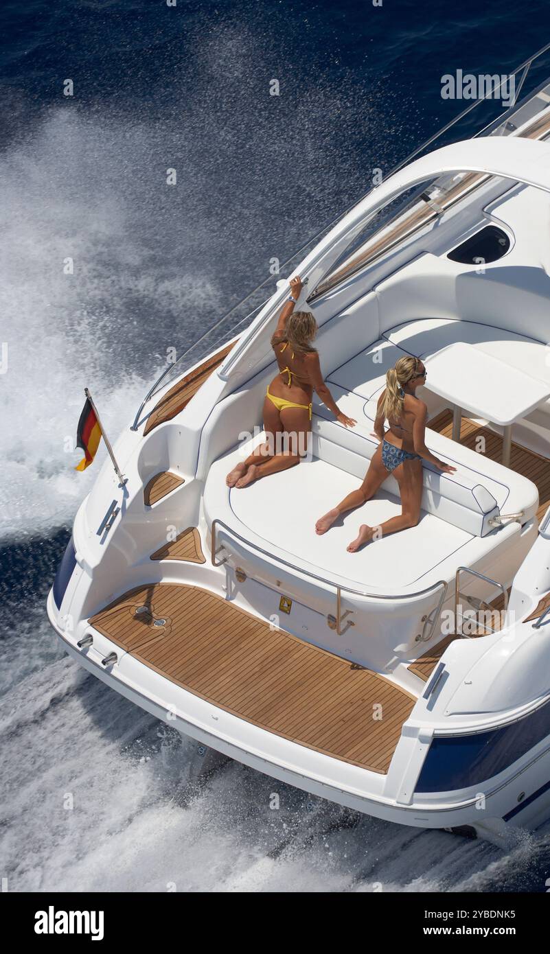 Photo aérienne de Bavaria Powerboat at Speed avec deux filles sur les chaises longues sur une mer bleu profond dans le soleil. Banque D'Images