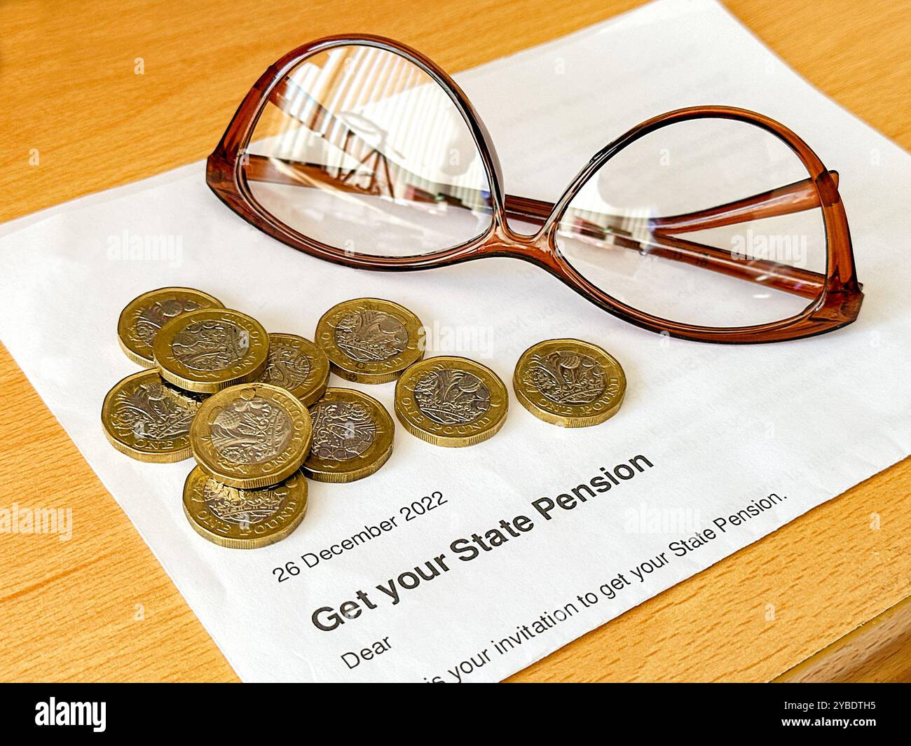 Lettre officielle disant à une personne en âge de retraite d'État au Royaume-Uni qu'ils peuvent obtenir leur pension, avec des pièces d'une livre et une paire de lunettes de lecture. - Image de stock capturée avec un smartphone