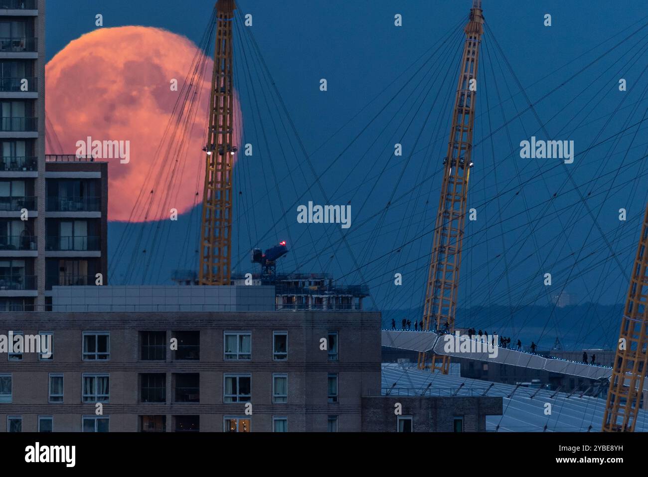 Londres, Royaume-Uni. 18 octobre 2024. Météo britannique : Super Hunter’s Moon se lève au-dessus de la ville. Les grimpeurs (en bas à droite) sont éclipsés par la lune massive alors qu'ils traversent le toit de la London O2 Arena. La pleine Lune d’octobre, connue sous le nom de Lune du chasseur, est également une Supermoon qui se produit lorsque la Lune est la plus proche de la Terre, apparaissant plus grande et plus lumineuse que la normale - jusqu’à 15% plus lumineuse et 30% plus grande. Cette année, la Lune paraîtra pleine pendant environ trois jours et sera la plus brillante de toutes les superlunes cette année. Crédit : Guy Corbishley/Alamy Live News Banque D'Images