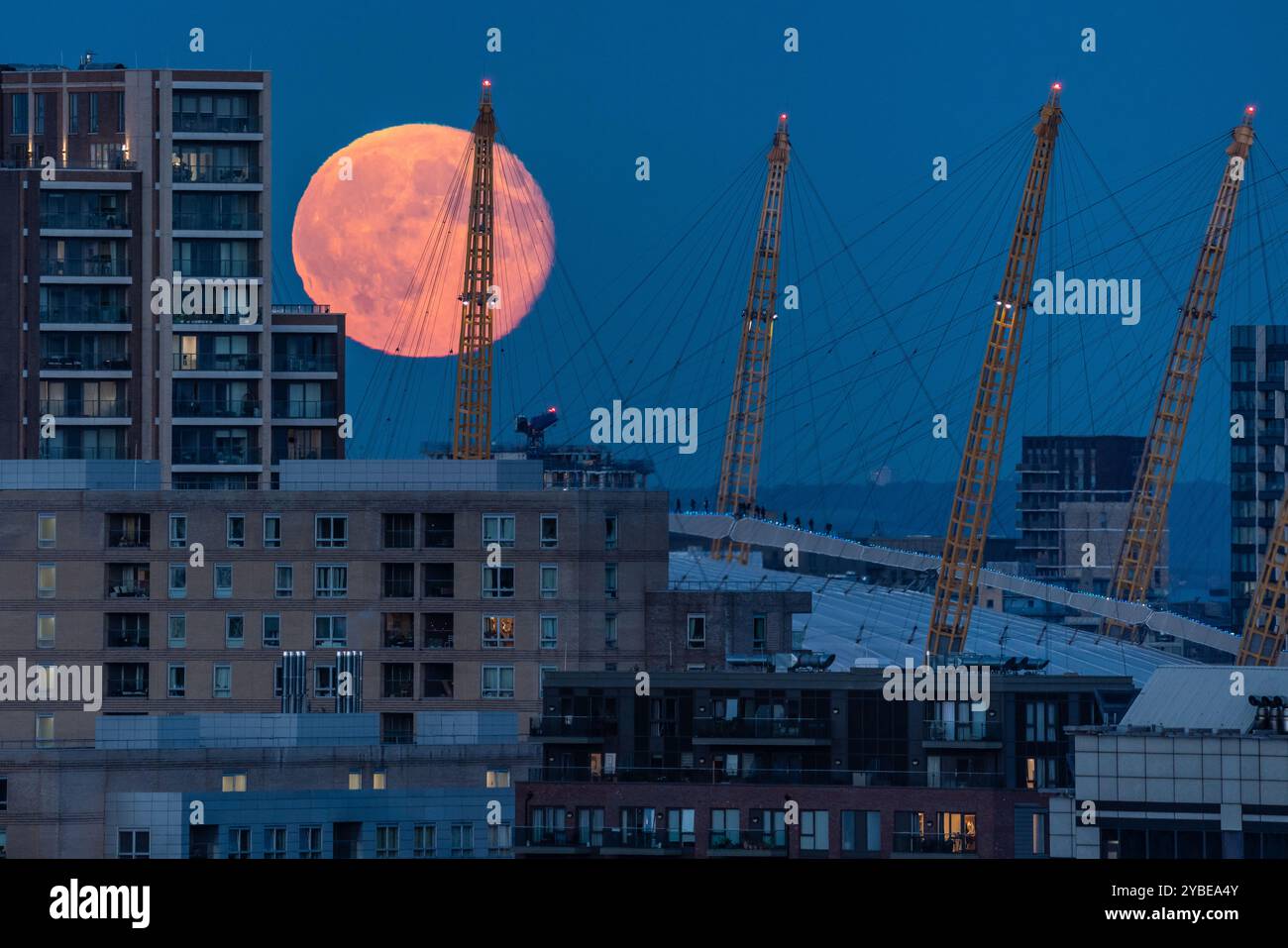 Londres, Royaume-Uni. 18 octobre 2024. Météo britannique : Super Hunter’s Moon se lève au-dessus de la ville. Les grimpeurs (au centre) sont éclipsés par la lune massive alors qu'ils traversent le toit de la London O2 Arena. La pleine Lune d’octobre, connue sous le nom de Lune du chasseur, est également une Supermoon qui se produit lorsque la Lune est la plus proche de la Terre, apparaissant plus grande et plus lumineuse que la normale - jusqu’à 15% plus lumineuse et 30% plus grande. Cette année, la Lune paraîtra pleine pendant environ trois jours et sera la plus brillante de toutes les superlunes cette année. Crédit : Guy Corbishley/Alamy Live News Banque D'Images