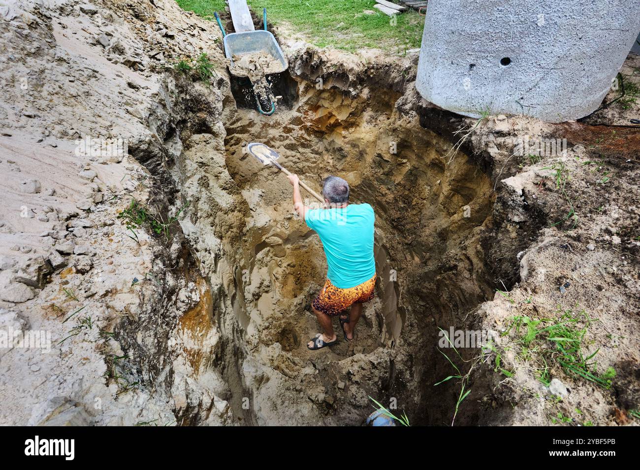 En creusant manuellement un trou pour fosse septique avec une pelle à baïonnette, le propriétaire jette de la terre dans la brouette. Banque D'Images