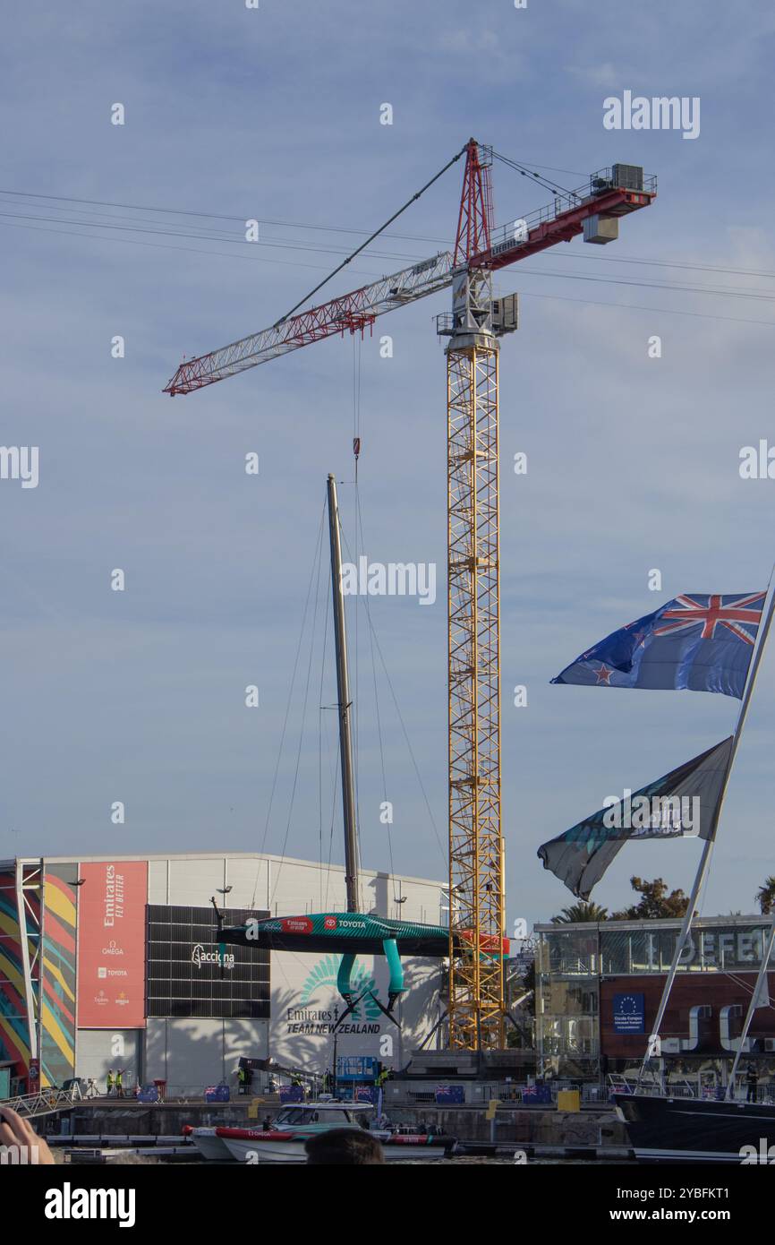 Barcelone, Espagne ; 12 octobre 24 : grue abaissant le navire Taihoro AC75 à terre pour effectuer la maintenance entre les régates de la Coupe de l'America. Des hydroptères sont vus. Banque D'Images