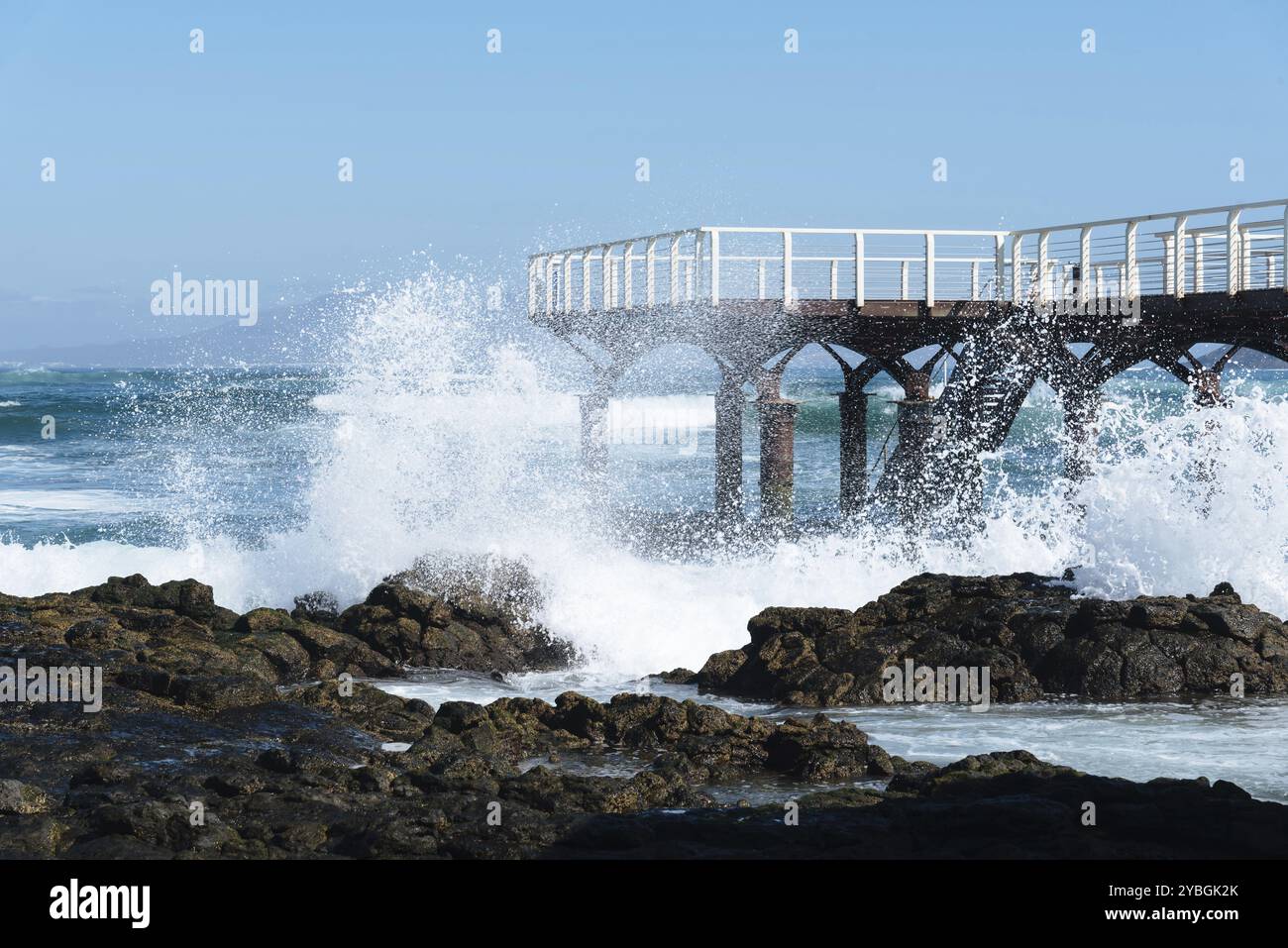 Les vagues se briser contre jetée sur la plage de Corralejo à matin contre le ciel bleu Banque D'Images