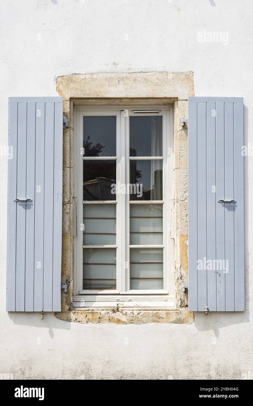 Vieille fenêtre en bois peint gris avec des volets ouverts sur le mur blanc d'hpuse traditionnelle dans l'île de Ré Banque D'Images