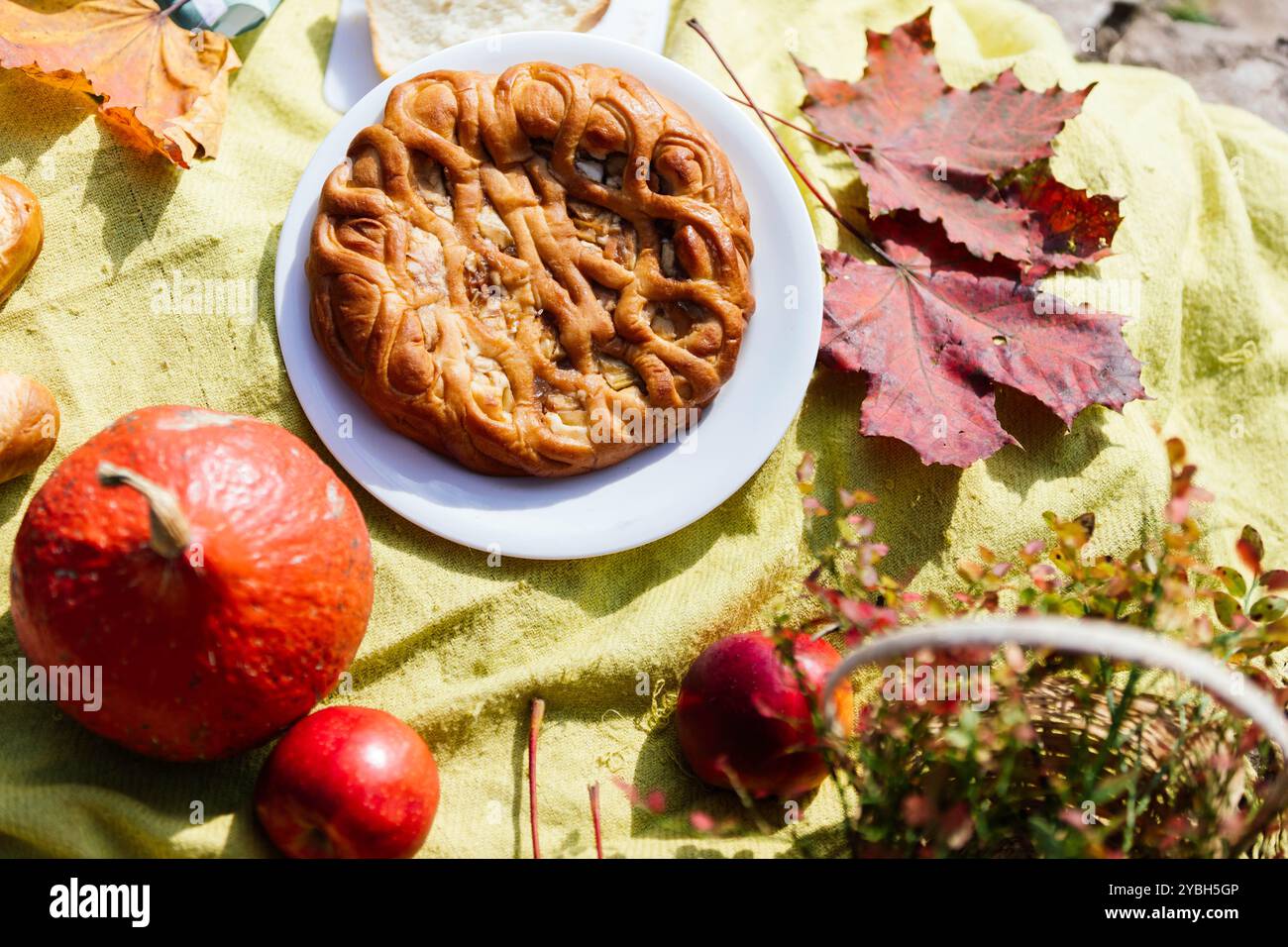 Un délicieux pique-nique d'automne est mis en place avec une pièce maîtresse de pâtisserie ronde, entourée de feuilles d'automne vibrantes, de citrouilles et de pommes sur un blanke doux et ensoleillé Banque D'Images