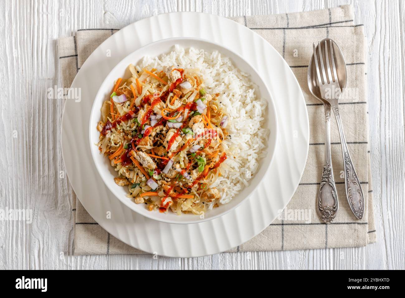 roulé aux œufs de tofu, chou sautés, tofu émietté assaisonné servi dans une sauce sucrée et salée servie sur du riz dans un bol sur une table en bois blanc avec fourchette Banque D'Images