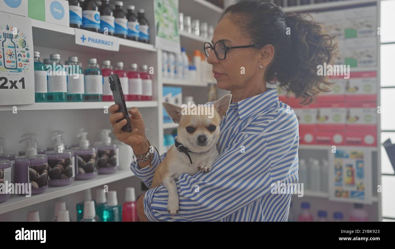 Une femme d'âge moyen tenant un chihuahua vérifie son téléphone dans une pharmacie. Banque D'Images