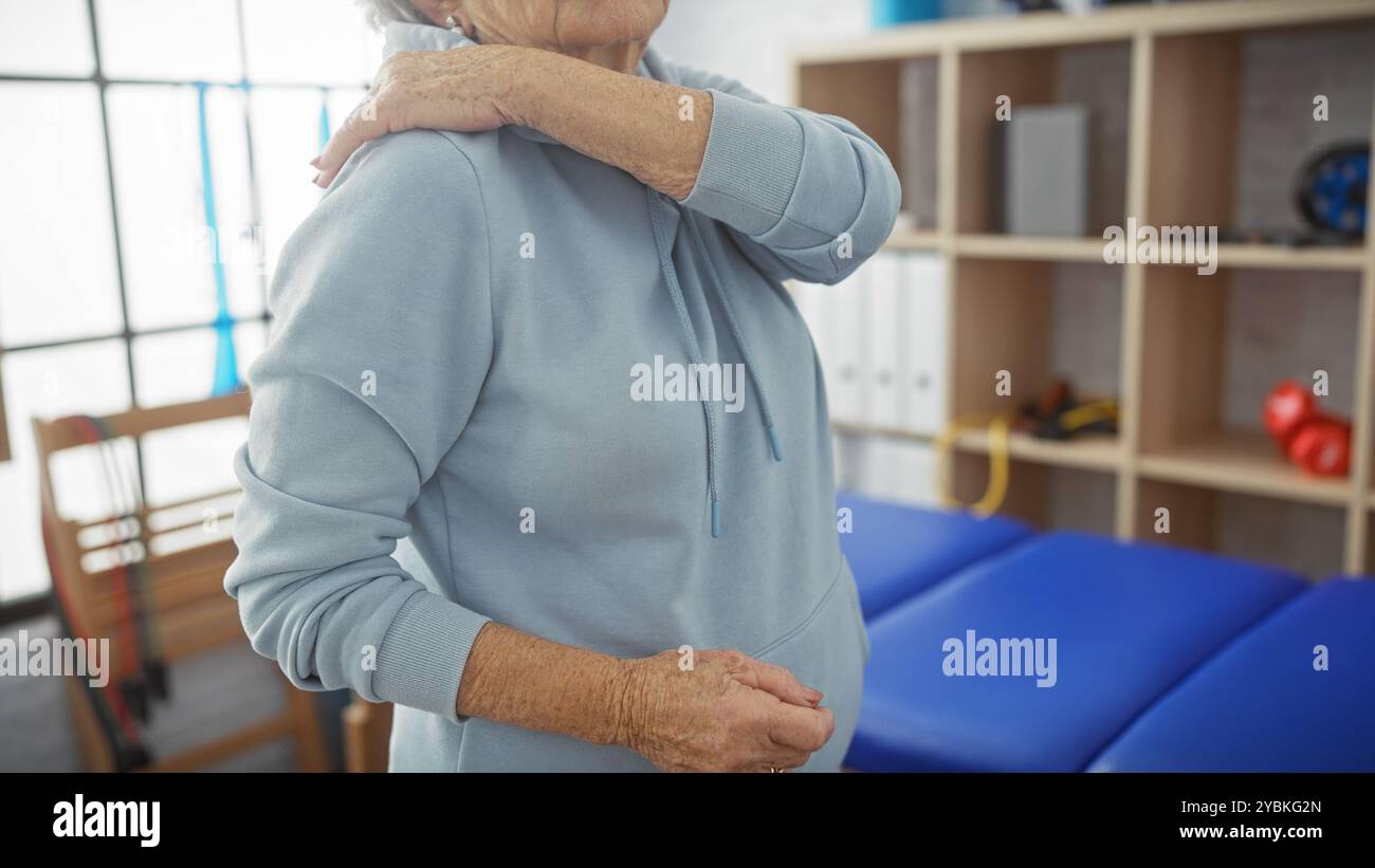 Une femme âgée ressent des douleurs à l’épaule lors d’une visite à une clinique de physiothérapie, transmettant un récit de soins de santé. Banque D'Images