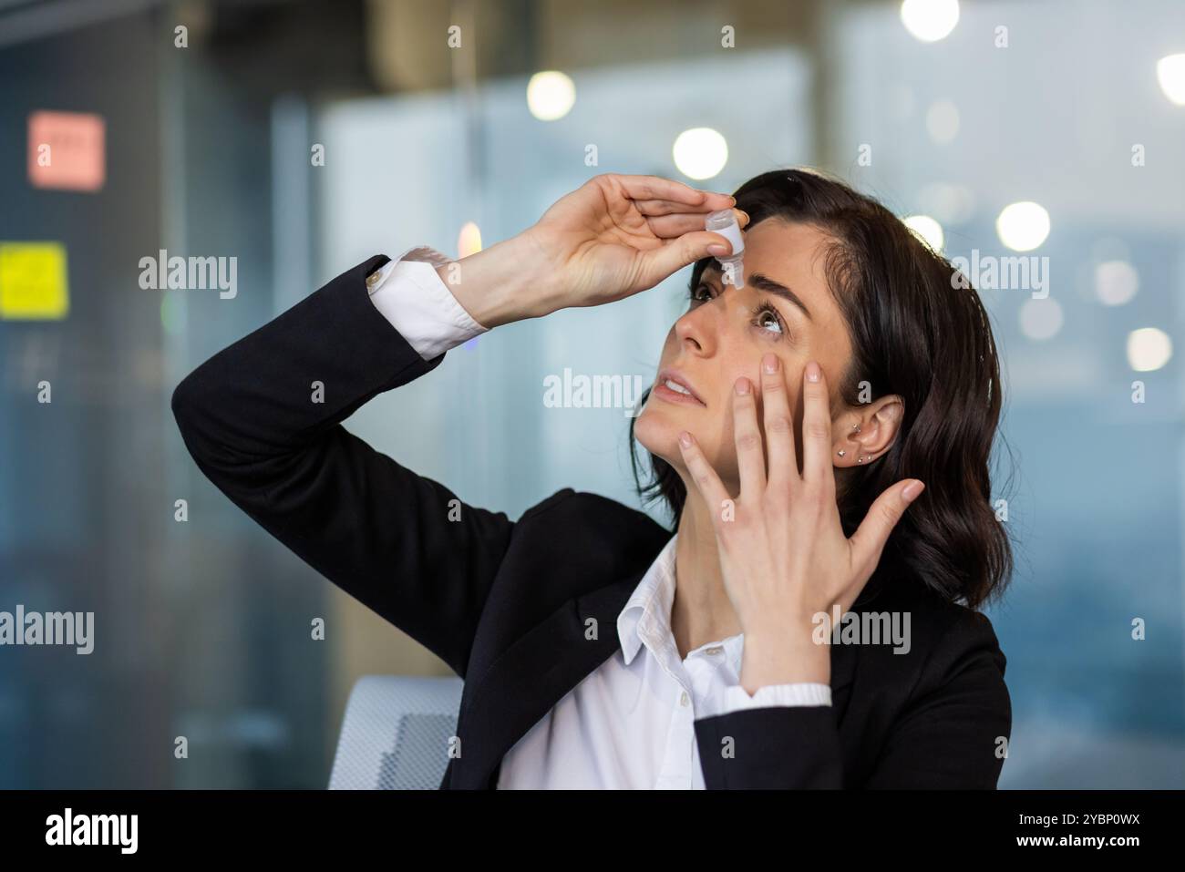 Femme d'affaires appliquant des gouttes pour les yeux secs. Concentrez-vous sur la santé et le confort dans un cadre professionnel. Assure une vision claire lors des réunions de travail importantes et des tâches de bureau. Banque D'Images