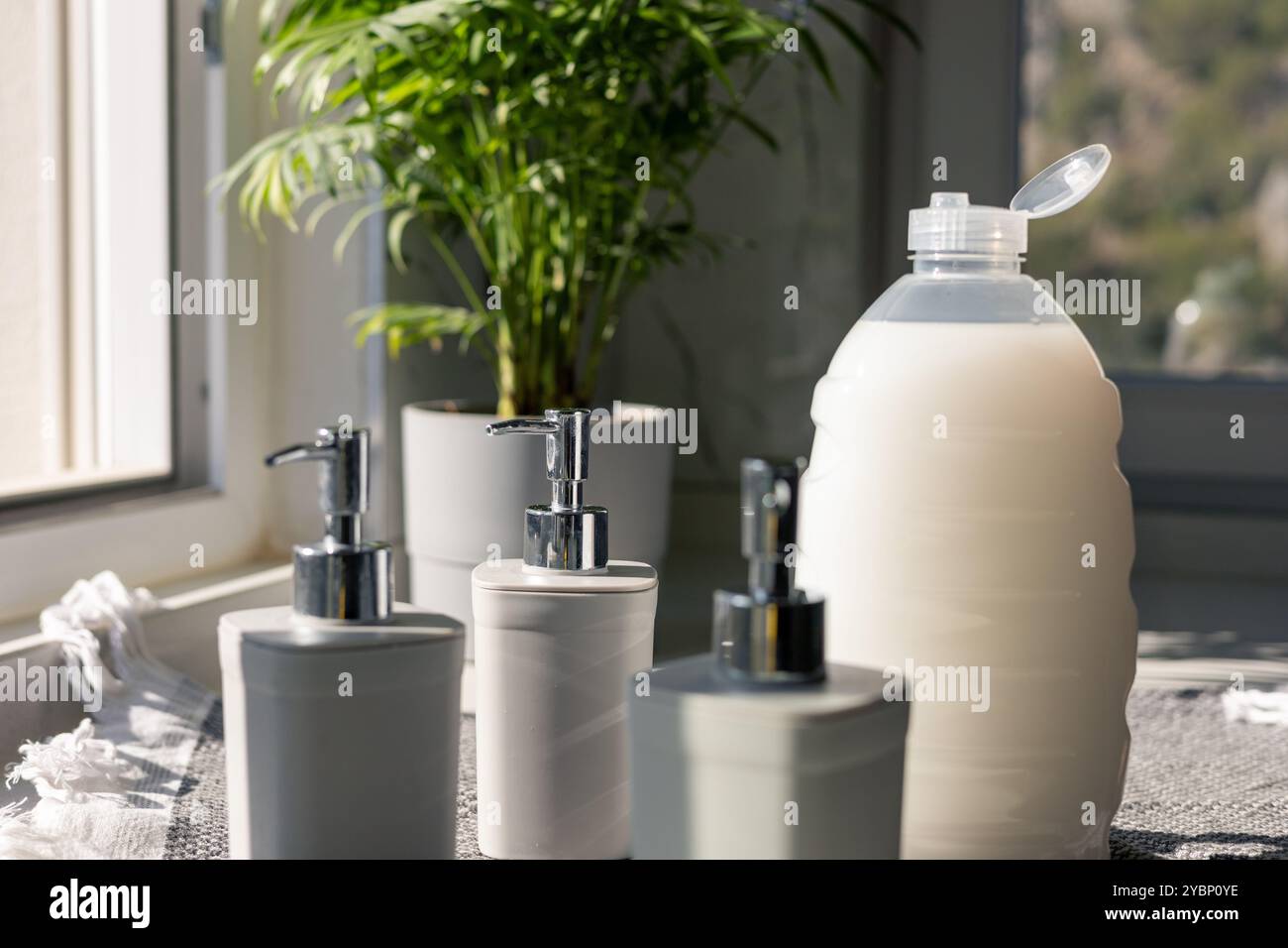 Comptoir de salle de bain élégant avec distributeurs de savon et une grande bouteille près d'une fenêtre Banque D'Images